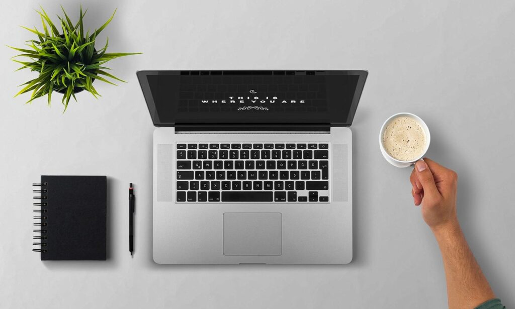 person updating LinkedIn profile on laptop with notebook and coffee nearby